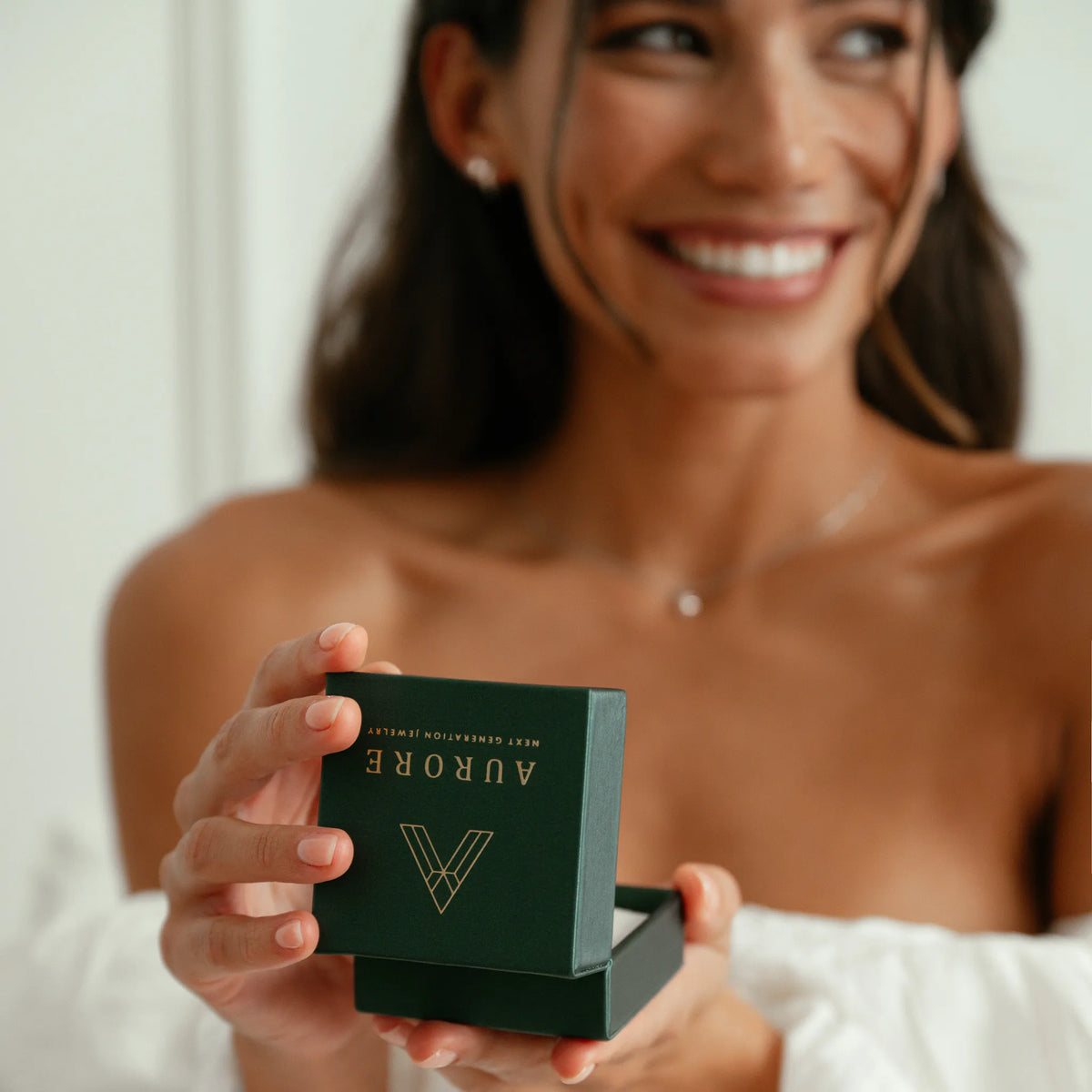 Lachende vrouw houdt een donkergroen sieradendoosje van Aurore Jewelry vast, klaar voor een bijzonder verlovingsmoment.